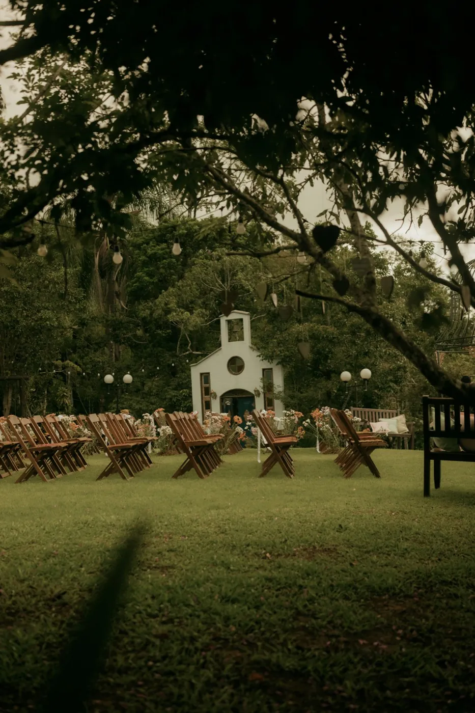 A garden ceremony: wooden chairs facing a small white chapel among trees