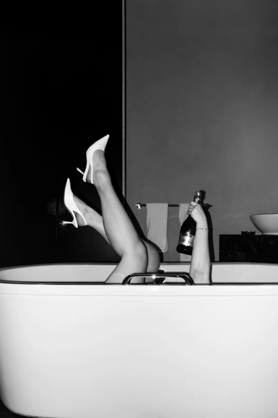 A playful black and white shot: bride's heels up from a bathtub, champagne in hand