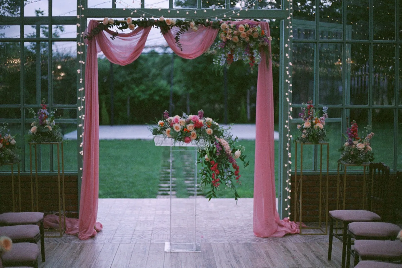 A greenhouse ceremony arch draped in rose fabric with string lights
