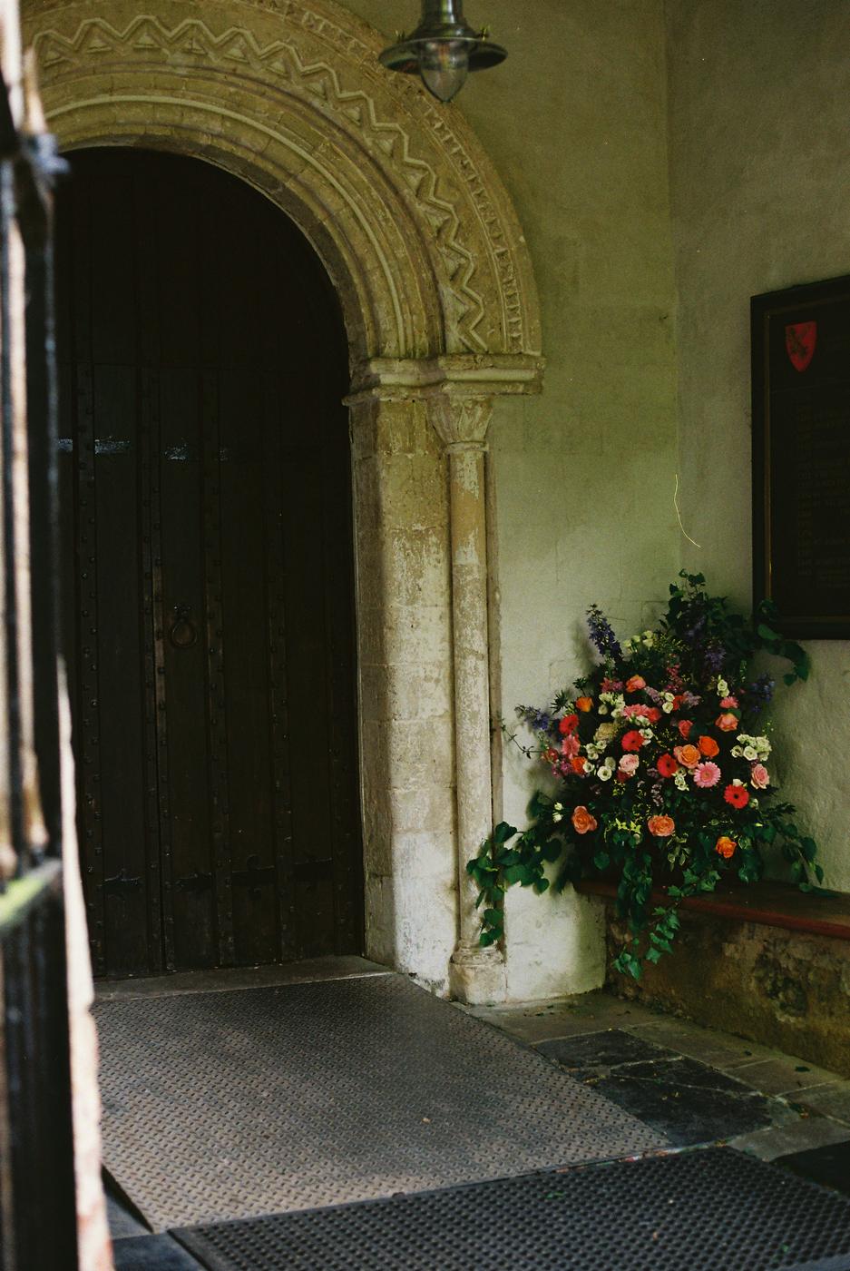 An old stone church doorway with a bright arrangement of roses and gerberas on the bench