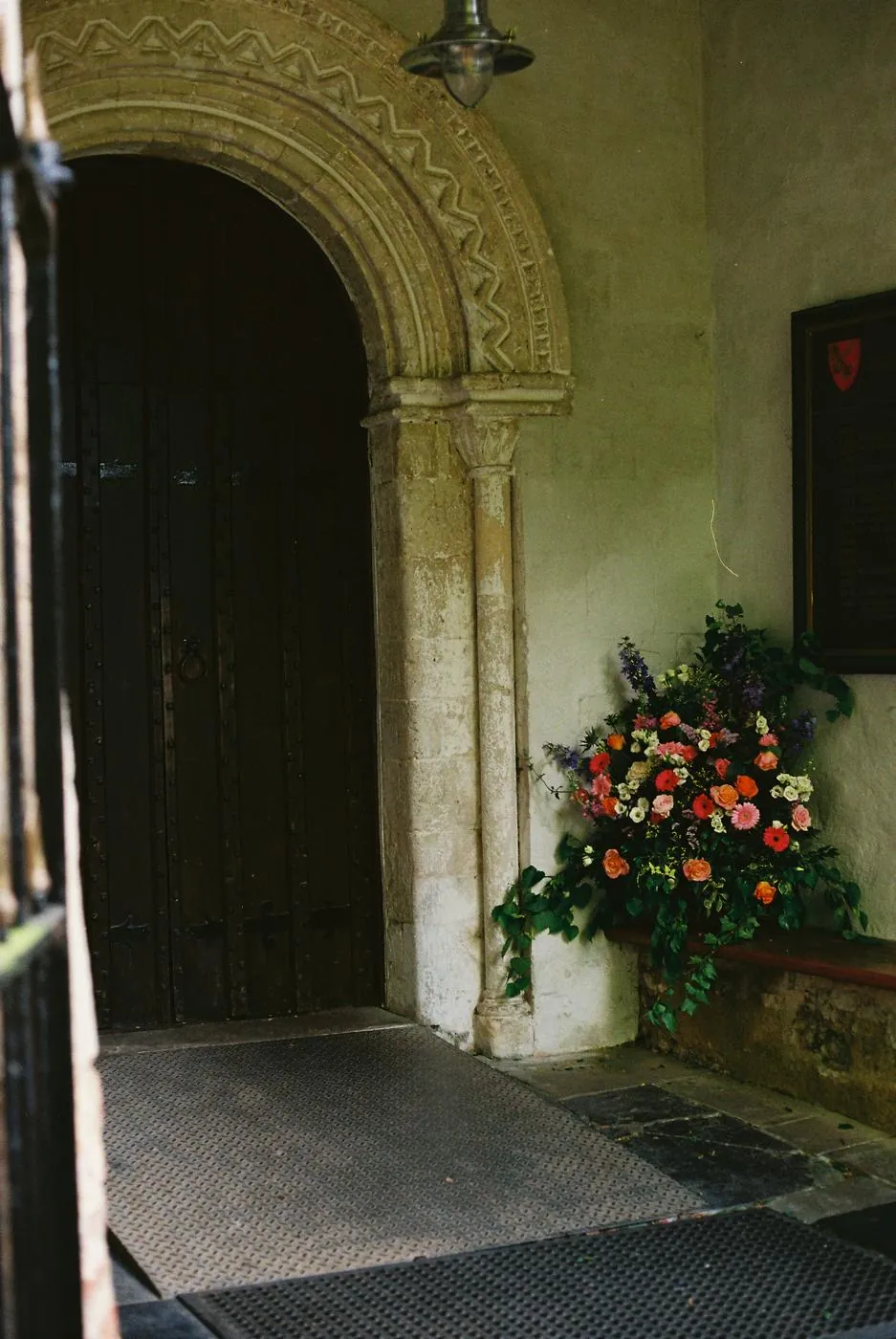 An old stone church doorway with a bright arrangement of roses and gerberas on the bench