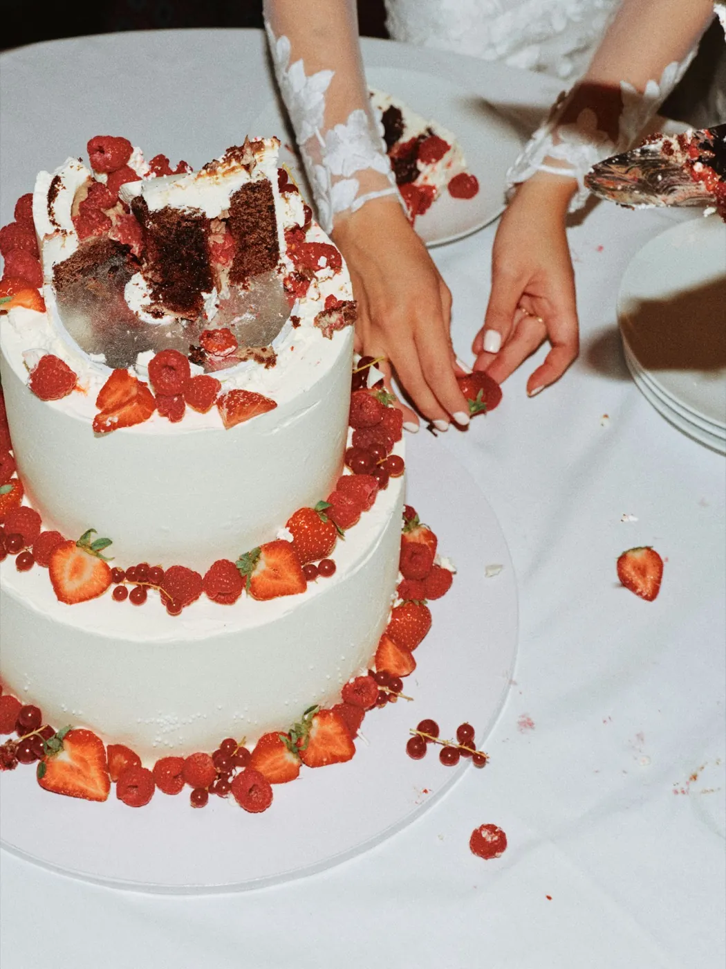 A bride's hands placing berries on a white two-tier wedding cake