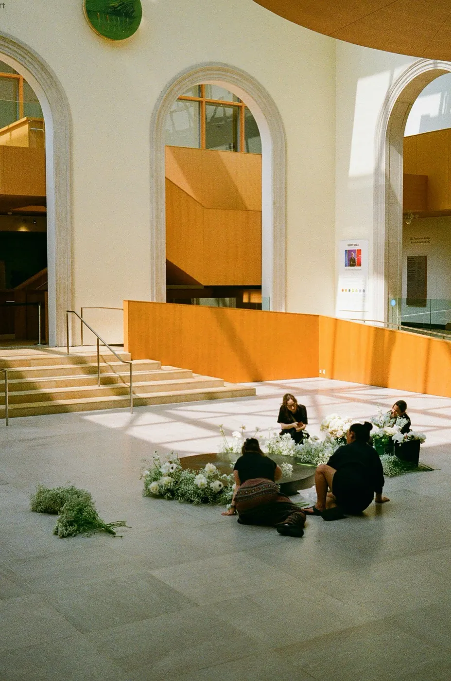 Florists arranging white flowers in a sunlit gallery atrium
